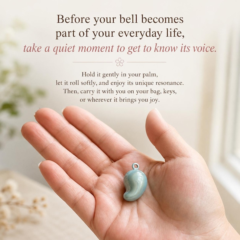 Może przedstawiać: Mały, gładki, jasnoniebieski dzwonek w kształcie kropli z metalowym k&oacute;łeczkiem na g&oacute;rze. Tekst głosi: Before your bell becomes part of your everyday life, take a quiet moment to get to know its voice. Hold it gently in your palm.
