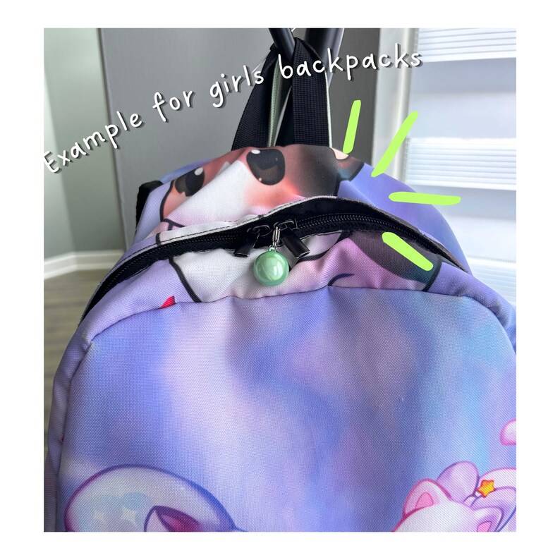 May include: A purple and blue gradient backpack featuring a cartoon character print and the text "Example for girls backpacks" in white. The bag has a black zip closure with a round, light green charm attached to the metal zip pull.