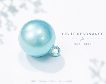 May include: A spherical, metallic light blue suzu bell with a small circular loop at the side. The text "LIGHT RESONANCE" and "SUZU BELL" is printed to the right, with the additional text "Light resonance for everyday moments." below.