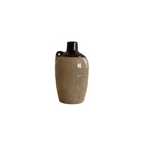 May include: A vintage ceramic jug with a brown top and handle, and a tan body. The jug has a classic, rounded shape and a small handle on the side. The jug is likely used for storing liquids.