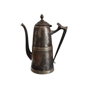 May include: A vintage silver coffee pot with a tall, slender body and a curved spout. The pot has a decorative handle and a lid with a small finial. Horizontal bands encircle the body. A classic piece for serving beverages, likely holding several litres.