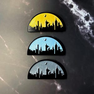 May include: Three semi-circular magnets with a cityscape silhouette design. Each magnet features a different color gradient: yellow, blue, and gray. A small bird silhouette is also included in each design. The magnets are black.