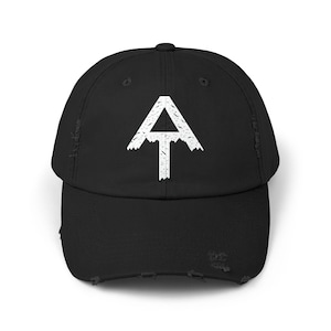 Op de afbeelding: Een zwarte, verweerde baseballpet met een wit Appalachian Trail-logo. Het logo is een gestileerde berg met een witte omtrek en een witte 'AT' erin.