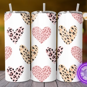 May include: Three white stainless steel tumblers with pink, tan, and black leopard print heart designs. Each tumbler has a silver lid and a matching straw. The tumblers are decorated with a repeating pattern of hearts.