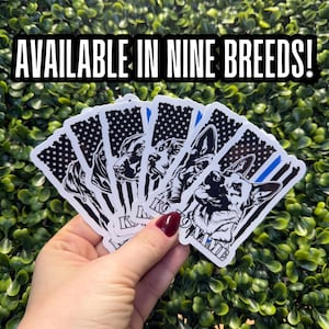 May include: A hand holds a stack of stickers featuring dog breeds with an American flag design. Each sticker has a black and white dog portrait and a blue line. The text "AVAILABLE IN NINE BREEDS!" is at the top.