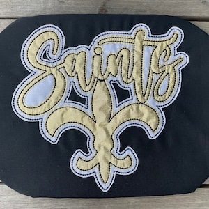 Puede incluir: Bolsa de tela negra con un lis bordado en oro y la palabra "Saints" en escritura dorada.