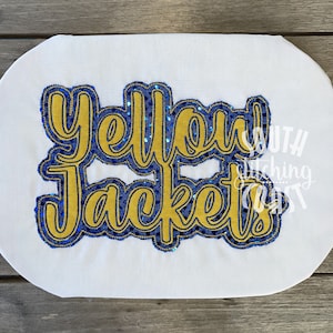 Pode incluir: Design bordado de "Yellow Jackets" com lantejoulas douradas e azuis sobre um fundo de tecido branco.