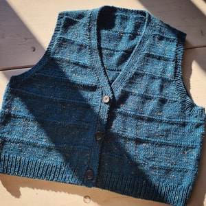 Może przedstawiać: Zielony, dzianinowy kamizelka z dekoltem w kształcie litery V i zapięciem na guziki. Kamizelka ma fakturę w kropki i poziome żebrowane wzory.