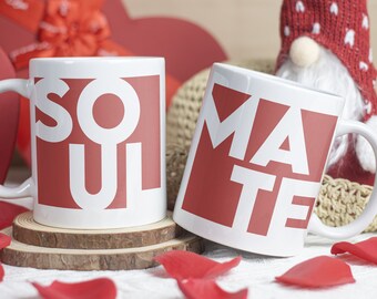 May include: Two white ceramic mugs with red accents. The mugs are on a white surface with rose petals. The mug on the left says "SOUL" and the mug on the right says "MATE".