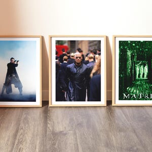 Peut inclure: Trois affiches encadrées du film Matrix. Les affiches présentent des images de personnages et de scènes du film, notamment des prises de vue d'action et la pluie numérique verte emblématique. Les cadres sont en bois clair.