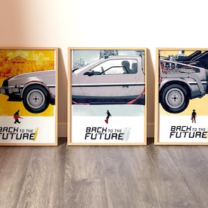 Puede incluir: Tres carteles enmarcados con el DeLorean de "Regreso al Futuro". Cada cartel muestra una vista diferente del coche, con el título de la película en la parte inferior. Los carteles están en marcos de madera.