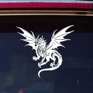 May include: White vinyl decal of a dragon with wings spread, on a black car window.