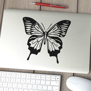 May include: A black and white silhouette of a butterfly on a white laptop.