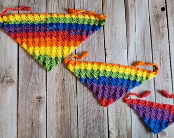 May include: Three rainbow crochet triangle scarves in different sizes. The largest scarf is red, orange, yellow, green, blue, purple, and red. The medium scarf is orange, yellow, green, blue, purple, and red. The smallest scarf is yellow, green, blue, purple, and red.