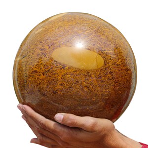 May include: A large, round, brown and gold sphere with swirling patterns. The sphere is being held in two hands.