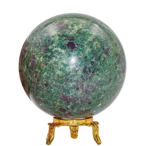 Puede incluir: Una gran esfera de piedra preciosa pulida, predominantemente verde con inclusiones granates, se asienta sobre un soporte decorativo dorado. La superficie de la esfera es lisa y reflectante, mostrando un patrón natural moteado. El soporte tiene un diseño ornamental de tres patas.