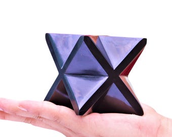 May include: A black and purple geometric star-shaped object made of wood. The object is being held in a person's hand.
