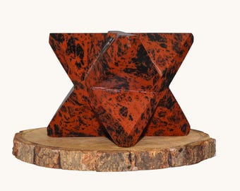 May include: A geometric star-shaped sculpture carved from polished mahogany obsidian with deep red and black mottled patterns. The object features multiple sharp, angular points and flat facets, showcasing a smooth, reflective surface texture.