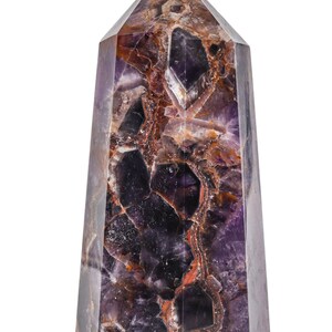 Puede incluir: Obelisco de cristal de amatista facetado. La piedra pulida presenta un tono púrpura intenso con inclusiones marrones y blancas. La forma geométrica y las variaciones de color del cristal crean un efecto visual llamativo, ideal para decoración.