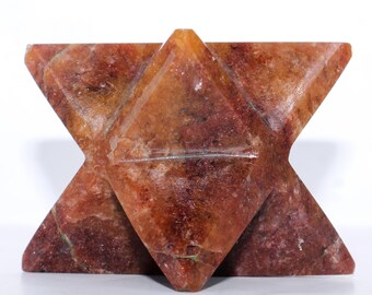 May include: A six-pointed star-shaped crystal carved from a reddish-brown stone. The crystal has a smooth, polished surface and is a natural, earthy color.