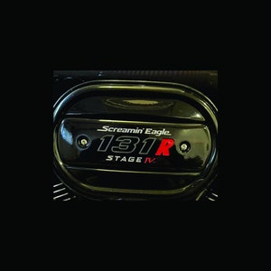 Puede incluir: Tapa de motor negra con un logotipo Screamin' Eagle 131R Stage IV en letras plateadas y rojas.