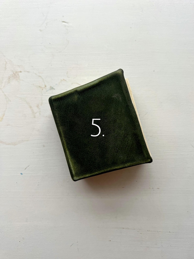 May include: A small, dark green book with a textured cover. The number "5" is printed in white on the cover. The book's pages are visible on the right side.