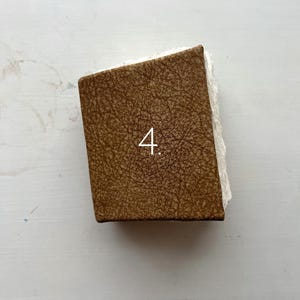 May include: A rectangular object with a brown, textured surface and the number "4" in white. The object has a rough, white edge on one side. The item is likely a decorative piece or a small box.