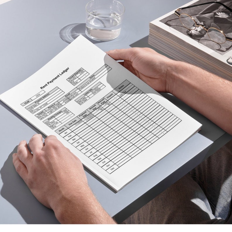 May include: A black and white rent payment ledger with columns for month, due date, payment due, amount paid, and notes. The ledger is on a gray surface.
