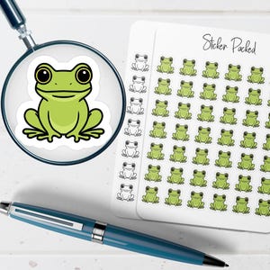 May include: A green frog sticker is magnified by a magnifying glass. A sheet of frog stickers and a blue pen are also in the image. The sheet of stickers has the text "Sticker Packed".