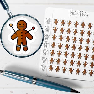 May include: A sheet of gingerbread man stickers with the text "Sticker Packed". A magnifying glass shows a close-up of a gingerbread man sticker with pins. A blue pen is in the foreground.