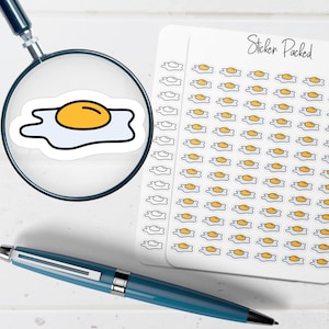 May include: A sheet of stickers featuring a fried egg design with a yellow yolk and white egg whites. The stickers are on a white background with the text "Sticker Packed" in cursive. A magnifying glass and a blue pen are also in the image.