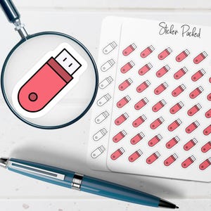 May include: A pink USB flash drive sticker is magnified by a magnifying glass. A sheet of stickers with multiple pink USB flash drive stickers is to the right. A blue pen is in the foreground. The text "Sticker Packed" is visible on the sticker sheet.