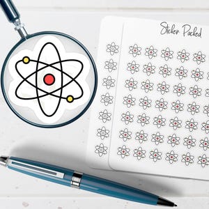 May include: A magnifying glass focuses on a sticker of an atom with a red center, yellow dots, and black lines. A sheet of stickers with atom designs and the text "Sticker Packed" is visible. A blue pen is in the foreground.