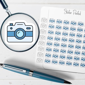 May include: A sheet of stickers with a repeating pattern of light blue and white camera illustrations. A single camera sticker is magnified by a magnifying glass. A blue pen is in the foreground. The text "Sticker Packed" is on the sticker sheet.