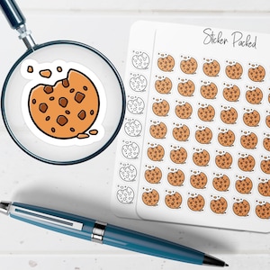 May include: A sheet of stickers with a repeating design of a bitten chocolate chip cookie. A magnifying glass focuses on a single cookie sticker. The words "Sticker Packed" are written on the sticker sheet. A blue pen is in the foreground.