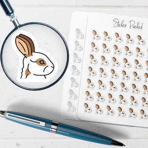 May include: A sheet of white stickers with a rabbit design, featuring brown ears and accents, with the text "Sticker Packed". A magnifying glass focuses on a single sticker. A blue pen is in the foreground.