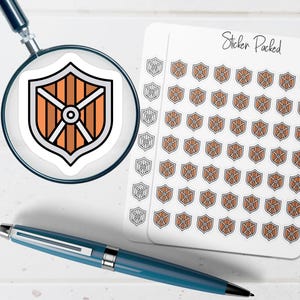 May include: A sheet of stickers featuring a shield design with orange and brown vertical stripes, a white and black border, and a central white circle. The stickers are labeled "Sticker Packed". A blue pen and magnifying glass are also in the image.