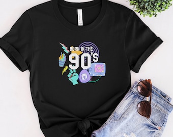 May include: Black t-shirt with a graphic design of a retro 90s theme. The design includes a boombox, a video game controller, a cup of iced coffee, and the text "Born in the 90s".
