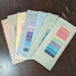 May include: A selection of colourful sticky note sets. Each set features rectangular sticky notes in various pastel shades, including pink, orange, yellow, blue, and purple. The packaging includes the text "Color Notes" and a ruler.