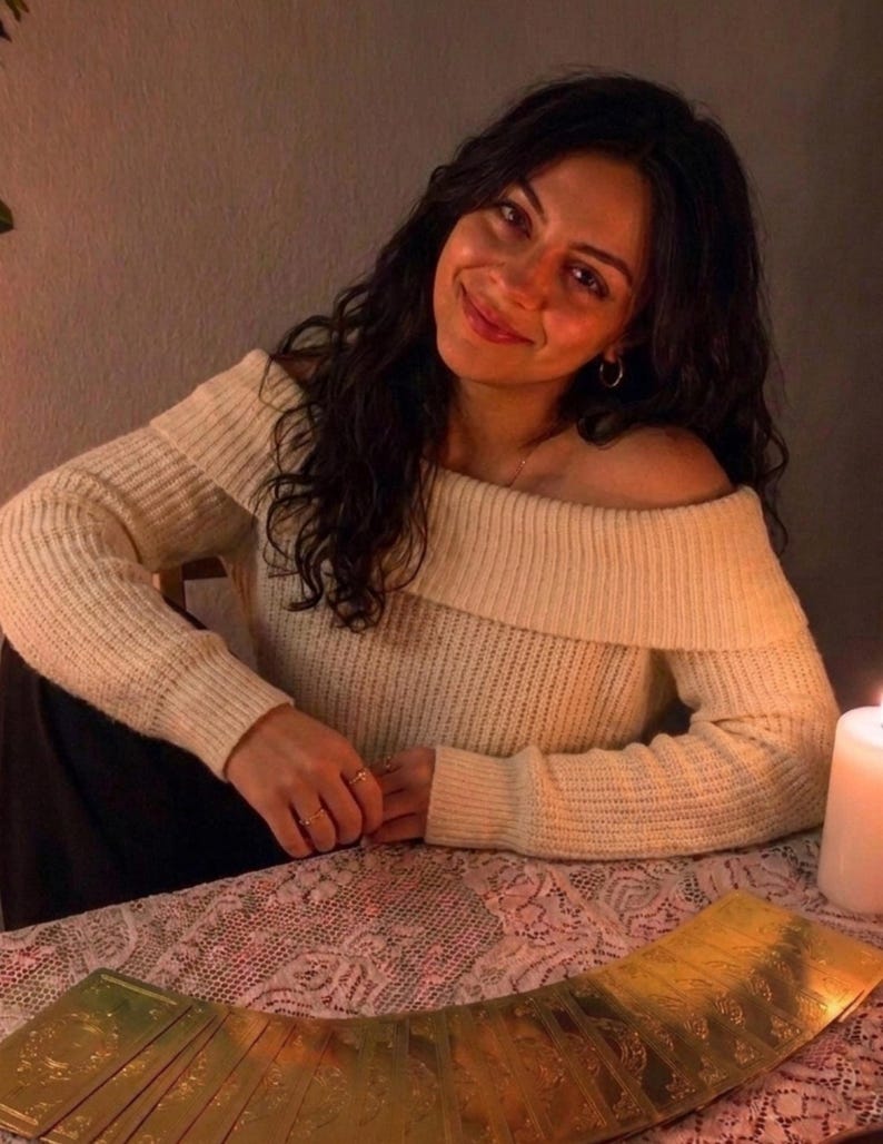 May include: An off-the-shoulder cream-colored ribbed knit sweater with long sleeves. The garment features a wide folded collar that rests across the shoulders and upper chest, providing a textured appearance with vertical ribbing throughout the fabric.