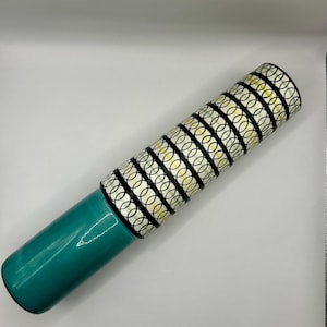 Op de afbeelding: Een cilindervormige, turquoise vaas met een patroon op het bovenste gedeelte. Het bovenste gedeelte heeft een herhalend ontwerp van zwarte, witte en gele in elkaar grijpende cirkels. De vaas is ongeveer 30 cm hoog.