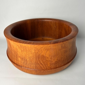 Peut inclure: Un saladier rond en bois de couleur brun rougeâtre chaud. Le bol a un large bord incurvé et une base légèrement évasée. Le grain du bois est visible, ajoutant de la texture. Ce bol décoratif est idéal pour servir ou exposer.