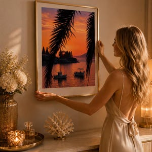 Könnte beinhalten: Ein gerahmter Kunstdruck, der einen Sonnenuntergang über einem ruhigen Gewässer mit zwei kleinen Booten zeigt, eingerahmt von den dunklen Silhouetten von Palmwedeln. Das Bild zeigt einen leuchtend orangefarbenen und violetten Himmel.