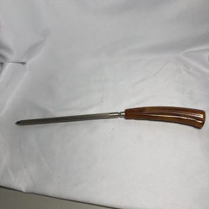 May include: A vintage knife sharpener. It features a long, slender steel rod and a curved handle. The handle is amber-coloured with a glossy finish. The sharpener is designed for sharpening knives and other cutting tools.