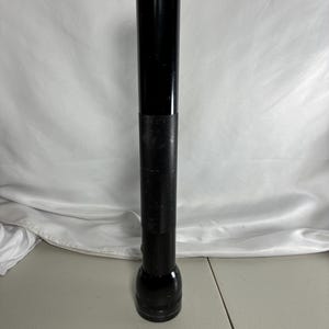 May include: A long, cylindrical black flashlight with a smooth upper barrel and a textured, knurled grip section in the middle. The head of the flashlight is wider than the body and features a flat, circular lens at the top end of the device.