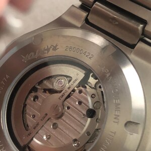 May include: Close-up of a silver titanium watch back, revealing the internal mechanism. The watch displays the text "TWENTY-ONE 21 JEWELS" and "MIYOTA JAPAN CHHJ". The serial number "28000422" is also visible.