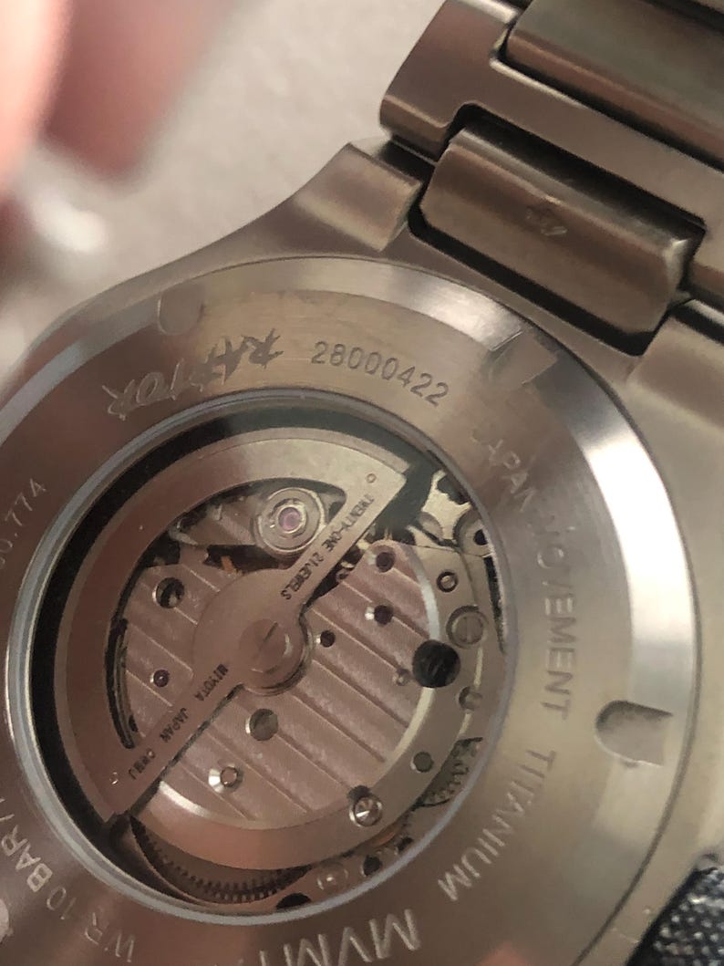 May include: Close-up of a silver titanium watch back, revealing the internal mechanism. The watch displays the text "TWENTY-ONE 21 JEWELS" and "MIYOTA JAPAN CHHJ". The serial number "28000422" is also visible.