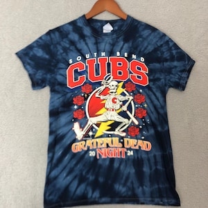 May include: A tie-dye t-shirt with a baseball-themed graphic. The design features the words "SOUTH BEND CUBS" in red and white, along with a skeleton baseball player. The shirt also includes the words "GRATEFUL DEAD 20 NIGHT 24" in orange.