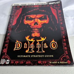 May include: A Diablo II Ultimate Strategy Guide by BradyGames featuring a black cover with a red, glowing skull illustration. The title Diablo II is printed in yellow with flame accents. Includes the ESRB Mature rating and author name.