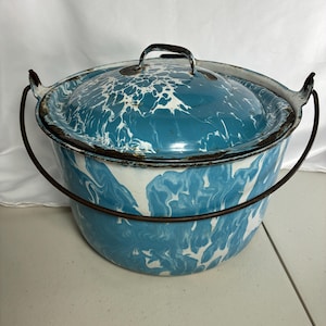 May include: A round, blue and white marbled enamel pot with a matching lid and a dark metal swing handle. The exterior features a swirling, cloud-like pattern in shades of blue and white, with visible dark metal edges showing signs of wear.